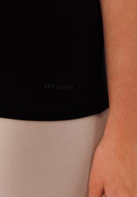 Černé tričko vyrobené z jemné látky, s malým, nenápadným logem "LES LUNES" na spodním lemu. Kombinováno se světle zbarvenými, přiléhavými legínami.