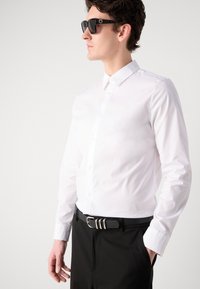 White button-up shirt with a classic collar, smooth texture, paired with a black belt featuring silver hardware, and black sunglasses.