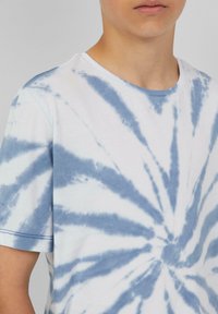 Witte katoenen T-shirt met blauw tie-dye spiraalpatroon. Korte mouwen en een ronde halslijn, met een zachte textuur en een ontspannen pasvorm.