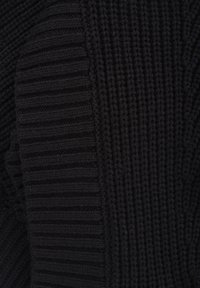 Pull en maille noire présentant une combinaison de motifs texturés et côtelés. Le tissu semble chaud et dense avec une finition lisse.