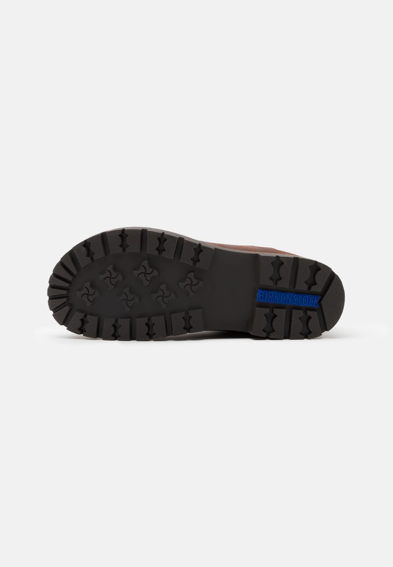 Birkenstock-Sohlen aus schwarzem Gummi mit tiefen Rillen und einer strukturierten Oberfläche. Blauer Logoakzent an der Ferse. Robustes und strapazierfähiges Design.