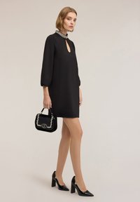 Czarna sukienka z dekoltem w kształcie łezki i ozdobnym kołnierzem. Dobrana do niej czarna torebka z srebrnymi akcentami oraz czarne buty na wysokim obcasie.