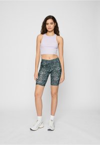 Top violet deschis scurt, cu design ajustat. Pantaloni scurți de ciclism verde închis, cu talie înaltă și model. Adidași albi sport și șosete.