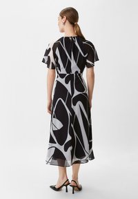 Czarna i biała sukienka w wzory z krótkimi, falbaniastymi rękawami i długością do połowy łydki. Posiada wycięcie w kształcie klucza na plecach oraz dopasowaną talię.