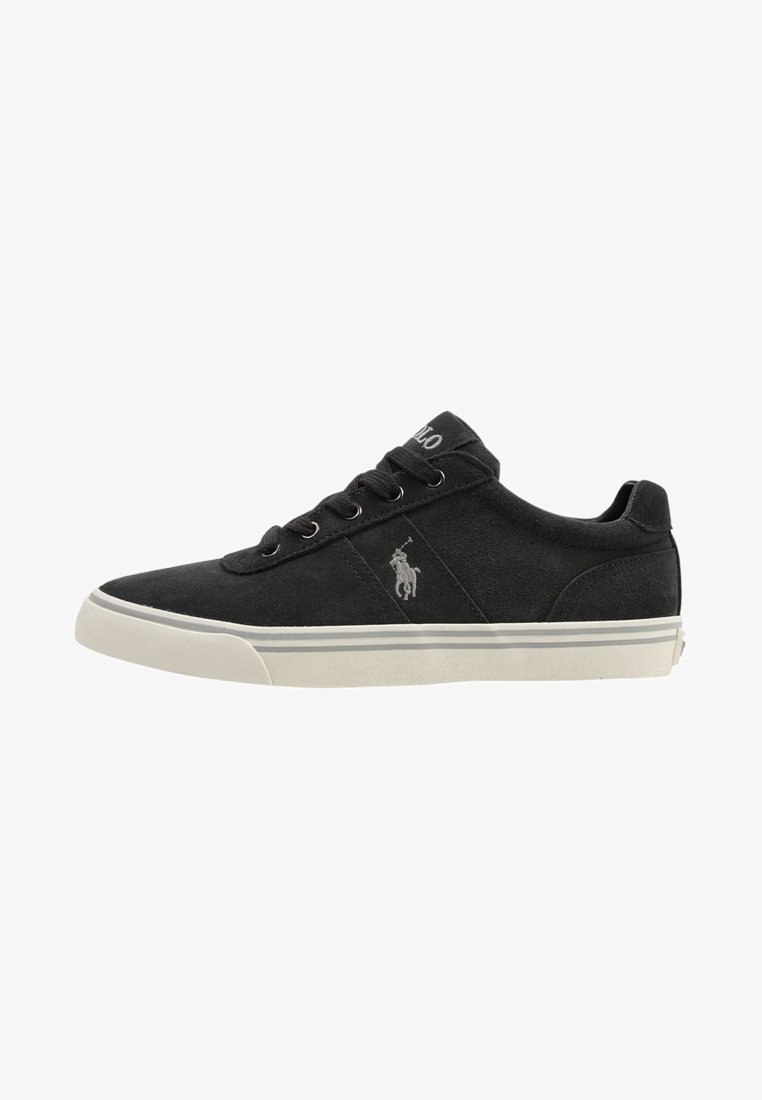Black suede sneakers with a white rubber sole, round toe, and lace-up design. Features a small grey logo on the side and striped accents.