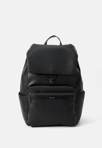 Sac à dos en cuir noir avec un rabat en haut, une poche frontale zippée et des poches latérales. Il est doté d'une poignée en boucle et d'une texture extérieure lisse.
