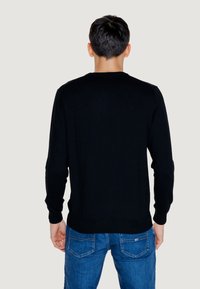 Maglione nero a maglia con collo rotondo classico, maniche lunghe e vita aderente. Indossato con jeans blu, presenta un design semplice e pulito.