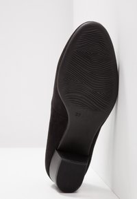 Chaussure noire en daim à petit talon reposant sur le côté, montrant une semelle texturée avec le marquage de taille 37 sur un fond blanc.