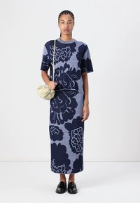 Abito in maglia con motivo floreale blu, maniche corte e silhouette dritta. Abbinato a una borsa beige e scarpe nere.