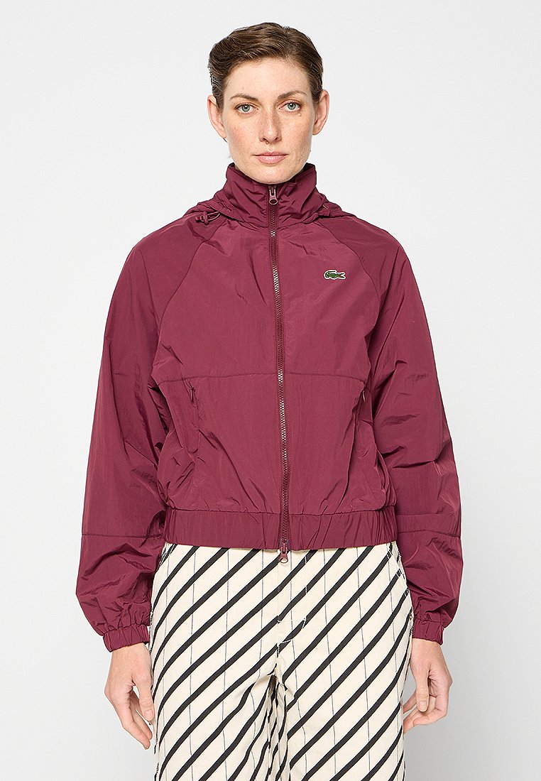 Bordeaux lichtgewicht jack met een hoge kraag en een frontale ritssluiting. Beschikt over elastische manchetten en een klein Lacoste-logo op de linkerbovenborst.