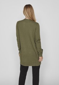 Olive green long cardigan in soft knit material, featuring ribbed cuffs and hem, with side slits for ease of movement.
