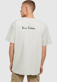 Hvid bomulds t-shirt med en løs pasform, korte ærmer og et håndskrevet "Viva la Vida" grafisk tryk i mørkegrå på ryggen.