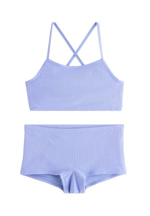 Vaaleanvioletti ribbikuminen kaksiosainen uimapuku, jossa on ristiin menevät ohuet olkaimet ja siihen sopivat poikashortsityyliset alaosat.