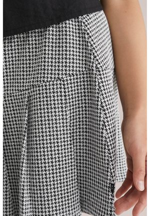 Jupe à motif pied-de-poule noir et blanc avec un tissu texturé, présentant une taille ajustée et des fentes latérales discrètes pour plus de liberté de mouvement.