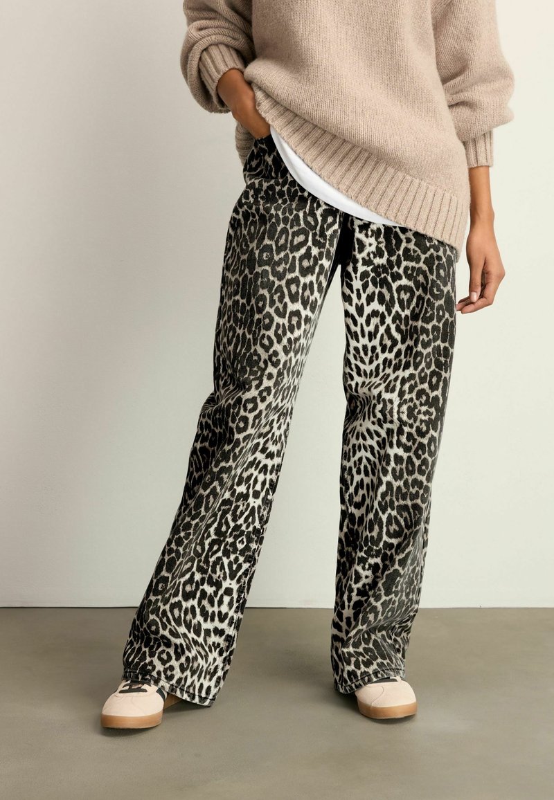 Hoch-taillierte, weite Hosen in Grau mit einem schwarzen Leopardenmuster, aus weichem Material. Kombiniert mit einem beigen Strickpullover und hellen Schuhen.