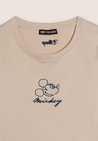 T-shirt côtelé rose clair avec un motif brodé de Mickey Mouse en bleu et le texte "Mickey", dotée d'un col rond et de manches courtes.