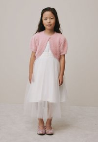 Rochie albă cu corset texturat și fustă din tull, asortată cu un cardigan roz pufos și pantofi roz strălucitori.