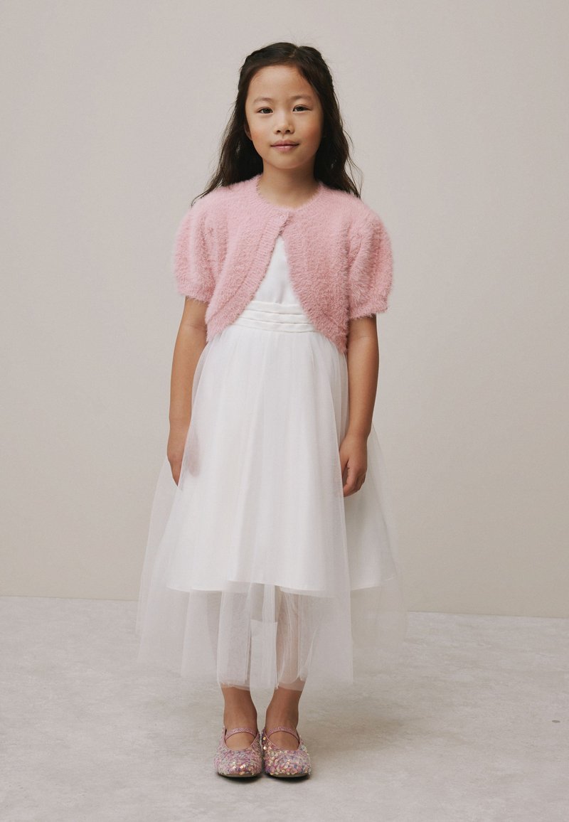 Rochie albă cu corset texturat și fustă din tull, asortată cu un cardigan roz pufos și pantofi roz strălucitori.