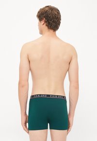 Grüne Baumwoll-Boxershorts mit einem schwarzen Bund, der den Text "PIER ONE" in Weiß trägt. Das Design ist einfach und figurbetont.