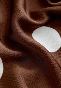 Tissu marron avec une surface texturée, présentant de grands pois blancs. Le matériau semble doux et tombe en vagues douces.