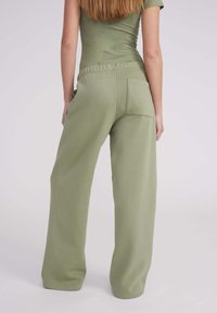 Pantalons de jogging vert clair fabriqués en tissu doux, avec une coupe décontractée, une taille élastique et une poche arrière du côté droit.