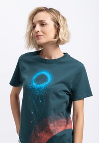 Teal katoenen t-shirt met een blauwe cirkelvormige graphic met spetters en vloeiende lijnen, aangevuld met een rood gebogen designelement.