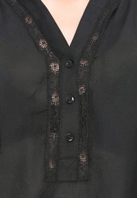 Sort bluse med V-hals, blondepanel kanter og fem matchende sorte knapper foran. Stof ser let og glat ud.