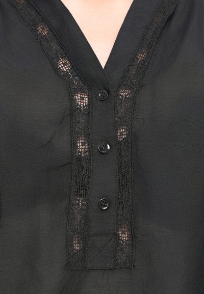Bluza neagră cu decolteu în V, cu o margine din dantelă și cinci butoane negre asortate pe față. Materialul pare ușor și neted.