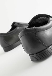 Chaussures en cuir noir avec une texture lisse, bout rond et semelle en caoutchouc basse. Présentent un détail de couture minimal et un design sans lacets.
