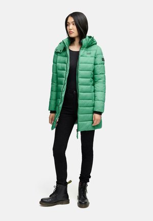 Green puffer jacket with a hood, quilted design, and front zipper. Worn over a black top and paired with black pants and boots.