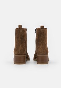 Botas de tobillo de ante marrón con una textura suave, punta redondeada y un tacón de madera grueso. Cremallera lateral para facilitar el uso.