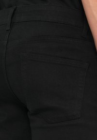 Jeans din denim negru cu o textură netedă, având un buzunar la spate și detalii de cusătură subtile. Croială clasică, conică, cu talie medie.