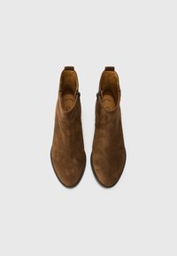 Bottes de cheville en suède brun avec une texture lisse, bout légèrement pointu, fermetures éclair sur les côtés et une languette à l'arrière pour un enfilage facile.