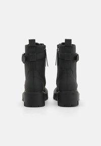 Bottines noires à cheville avec une finition mate et lisse. Dotées d'une semelle épaisse, de fermetures éclair latérales et de sangles ajustables à l'arrière pour un maintien sécurisé.