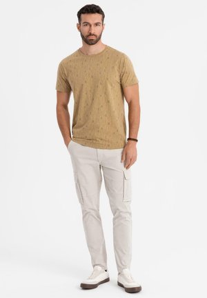 Camiseta de manga corta de color marrón claro con un patrón, combinada con pantalones cargo de color beige claro y zapatillas blancas, mostrando un ajuste relajado y bolsillos prácticos.