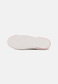 Biała podeszwa sportowa z teksturowanym gumowym gripem, z różowym akcentem na pięcie i falistym wzorem na spodzie dla lepszej przyczepności.