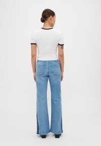 Hvit t-skjorte med korte ermer og marineblå detaljer, kombinert med høyhansete, lys blå svakt utvidede jeans. Jevnt stoff med synlige sømmer og lommer.