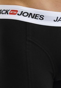 Crne pamučne bokserice s bijelim elastičnim pojasom na kojem je ispisano "JACK JONES" crnim slovima. Glatka tekstura i kroj koji se prilagođava tijelu.