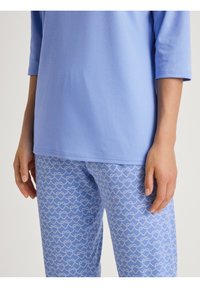 Lichtblauw katoenen t-shirt met driekwartmouwen, gecombineerd met gestreepte blauwe leggings met witte hartvormen op een zachte textuur.