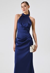 Navy Satin-Halter-Abendkleid mit drapiertem Design. Accessoires: eine beige Clutch mit strukturierter Oberfläche und Klappenverschluss.