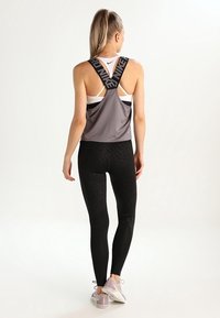Top de atletismo gris con tirantes cruzados en la espalda, combinado con leggings negros con un patrón texturizado, y zapatillas de deporte gris claro.