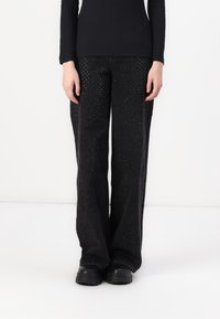 Pantalons noirs en tissu texturé, dotés d'une coupe droite avec de petites clous réfléchissants partout. Associés à des bottes noires robustes.