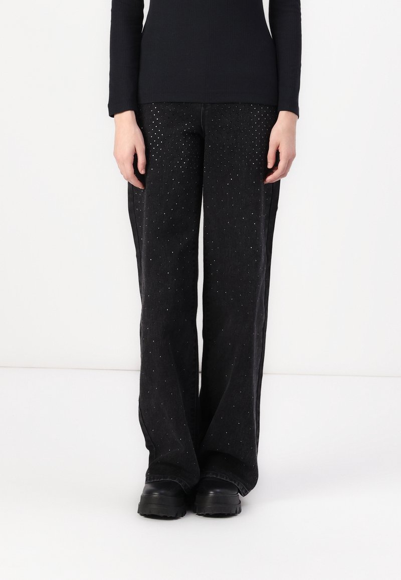 Pantalons noirs en tissu texturé, dotés d'une coupe droite avec de petites clous réfléchissants partout. Associés à des bottes noires robustes.