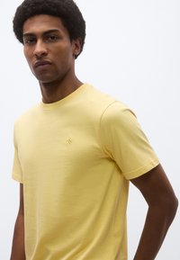 Κίτρινο t-shirt με στρογγυλή λαιμόκοψη από μαλακό βαμβάκι και κοντά μανίκια. Διαθέτει ένα μικρό κεντημένο λογότυπο στο πάνω αριστερό μέρος. Ομαλή υφή.