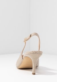 Chaussure slingback en cuir beige embossé crocodile avec un talon fin, dotée d'une boucle dorée et d'une doublure intérieure lisse.