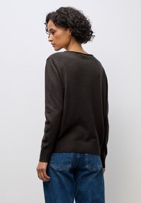 Dark brown sweater with a relaxed fit, ribbed hem and cuffs, paired with blue denim jeans, showcasing a simple and casual design.