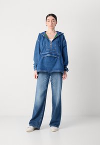 Denimtröja med halv dragkedja, huva och ficka fram, i kombination med vida denimbyxor. Ljusblå färg, av avslappnad design med dragsnören.