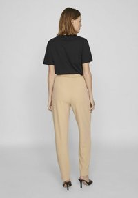 Zwarte t-shirt met korte mouwen gecombineerd met hoogwaist beige broek. De broek heeft een rechte snit en een gestructureerde stof; minimalistische esthetiek.