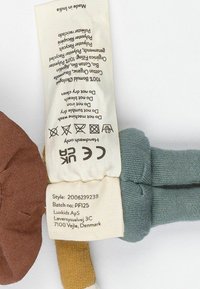 Etikett mit Pflegehinweisen für ein Stofftier aus beigefarbenem Stoff, mit schwarzem Text, der das Material und die Waschanleitungen beschreibt.