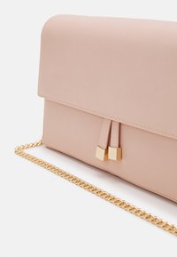Blush pink leather clutch with gold cube embellishments on tassels and a gold chain strap resting on a white surface.
